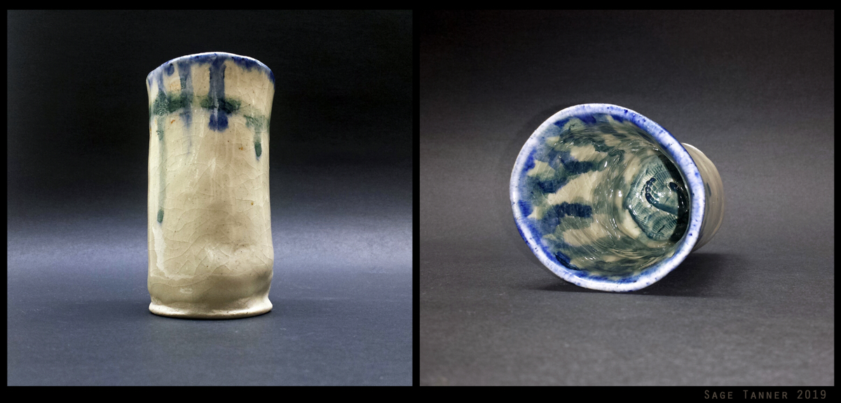 A hand-formed white ceramic cup with dripping blue stain and a miniature handprint on the inside.
